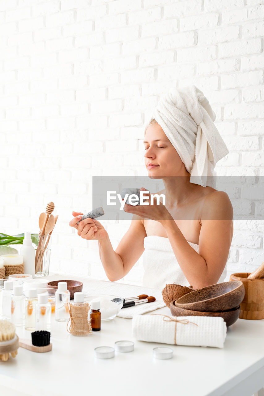 Happy young woman wearing white bathrobes towels on head doing spa procedures mixing natural 