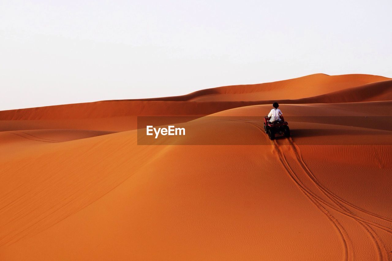 Rear view of man riding quad bike on sand dune against clear sky