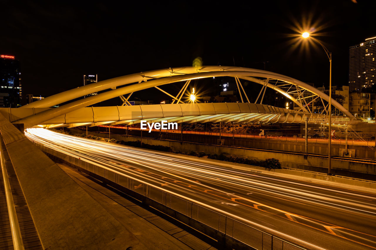 LIGHT TRAILS ON BRIDGE OVER STREET AT NIGHT