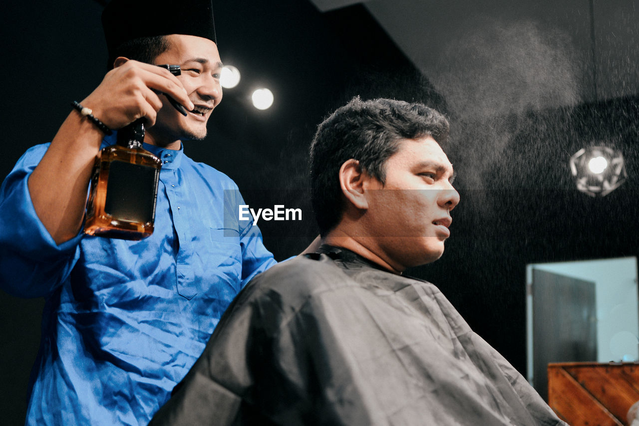 Smiling hairdresser spraying water on man head