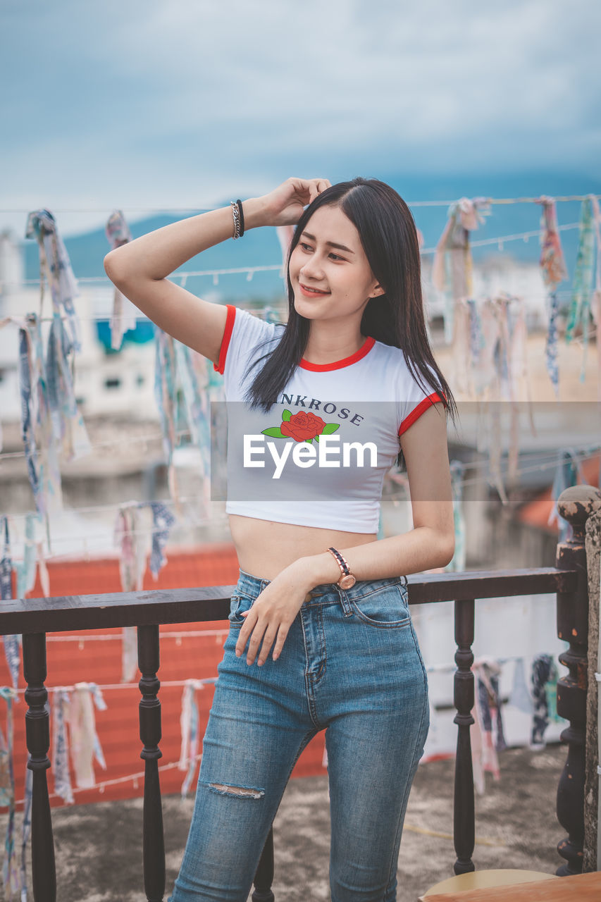 Smiling young woman standing against cloudy sky