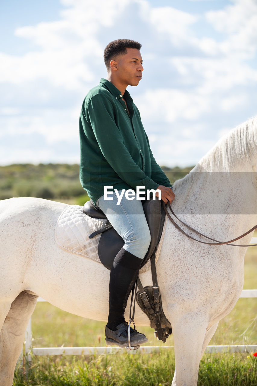 SIDE VIEW OF A YOUNG MAN RIDING HORSE