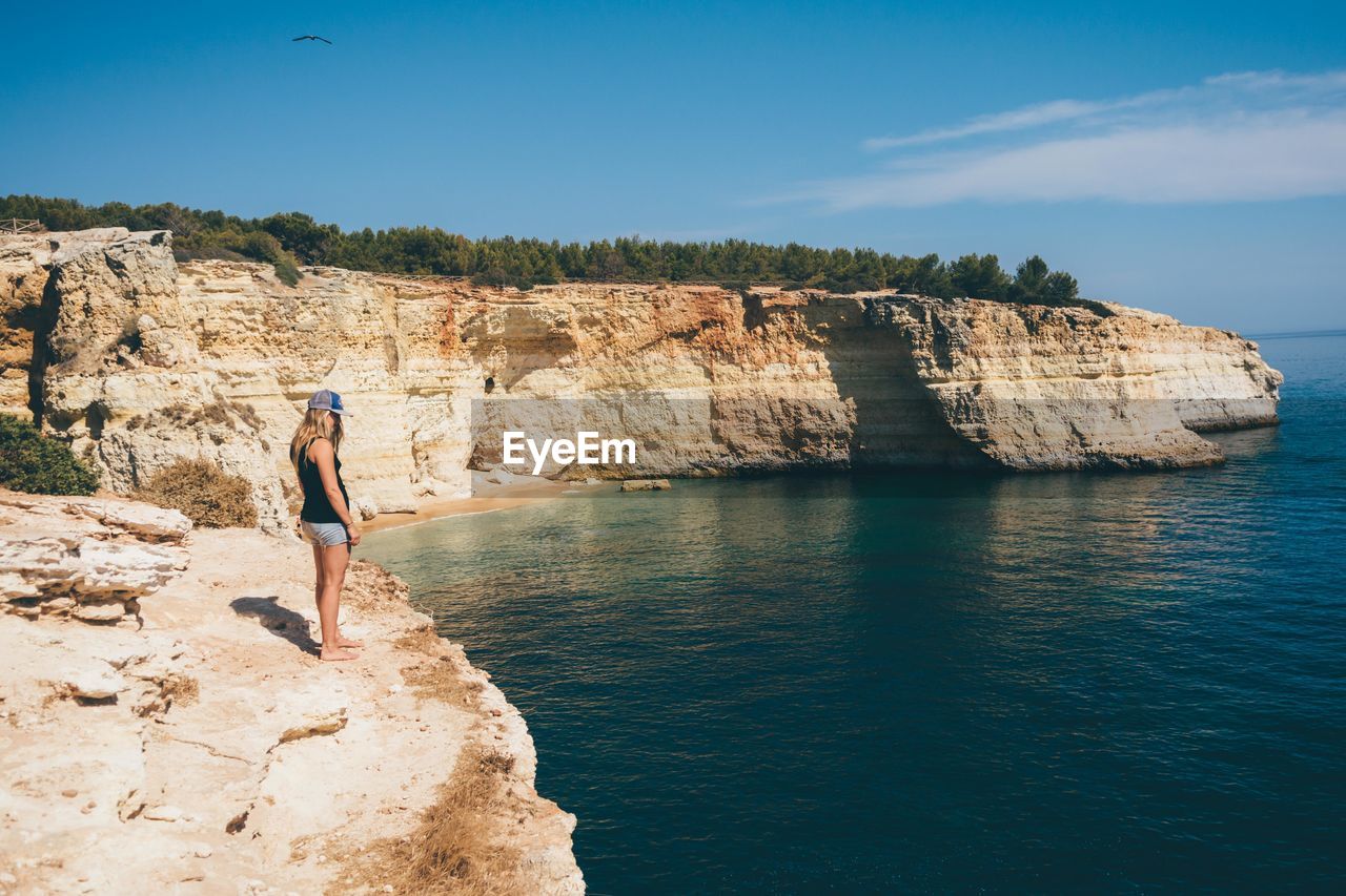 Side view of woman standing on cliff by sea