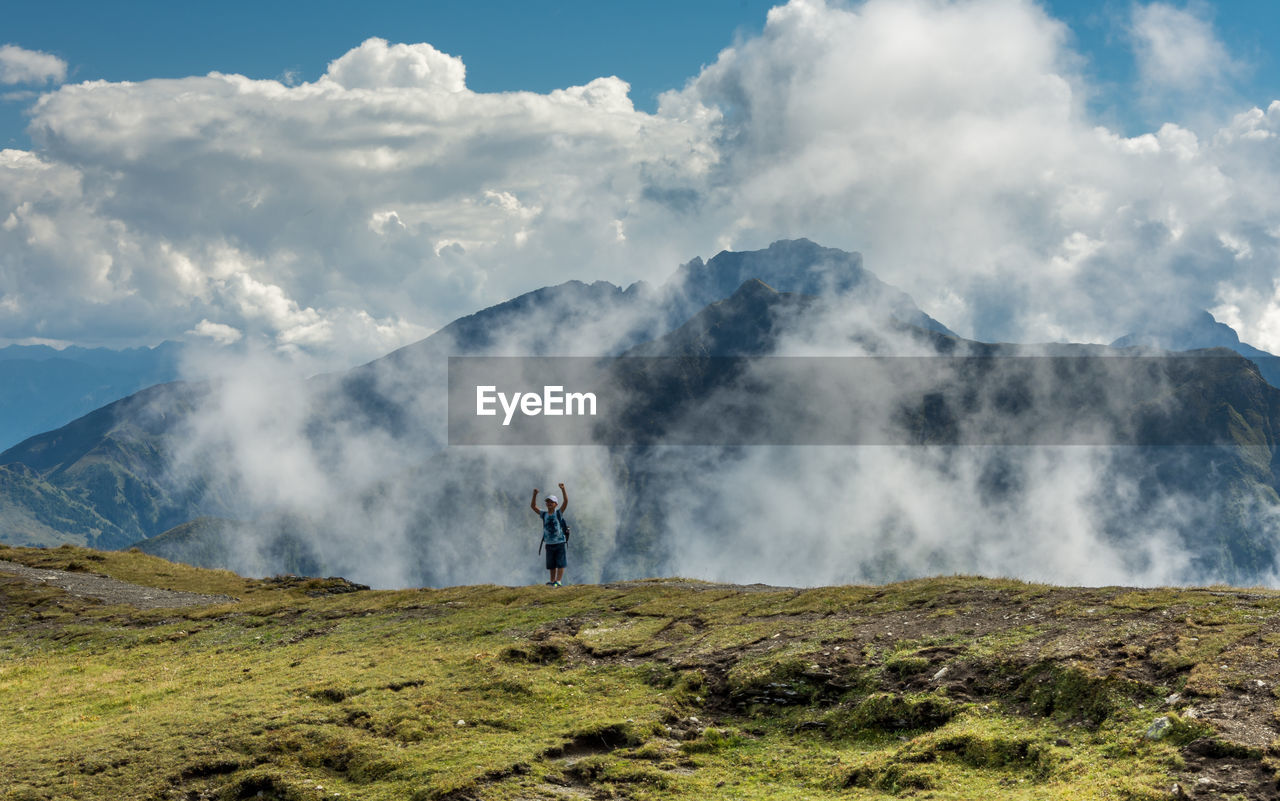 Excited man standing on mountain peak against sky