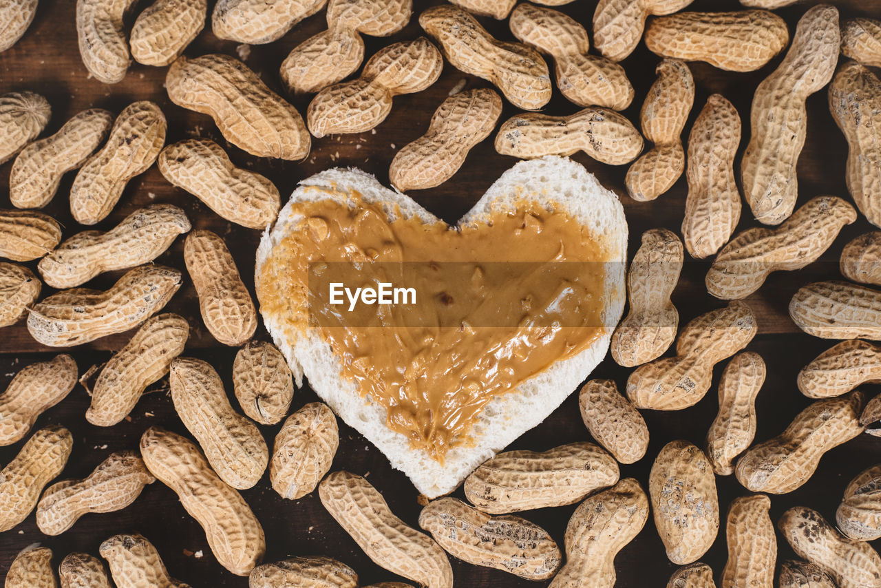 Top view of a peanut butter spread on white bread and groundnuts on wooden table.