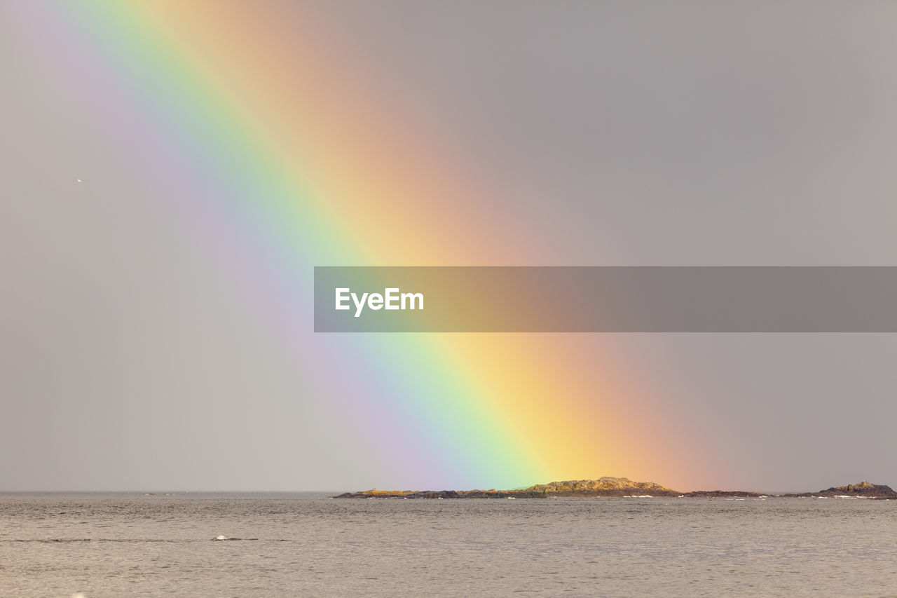 RAINBOW OVER SEA AGAINST SKY AT SUNSET