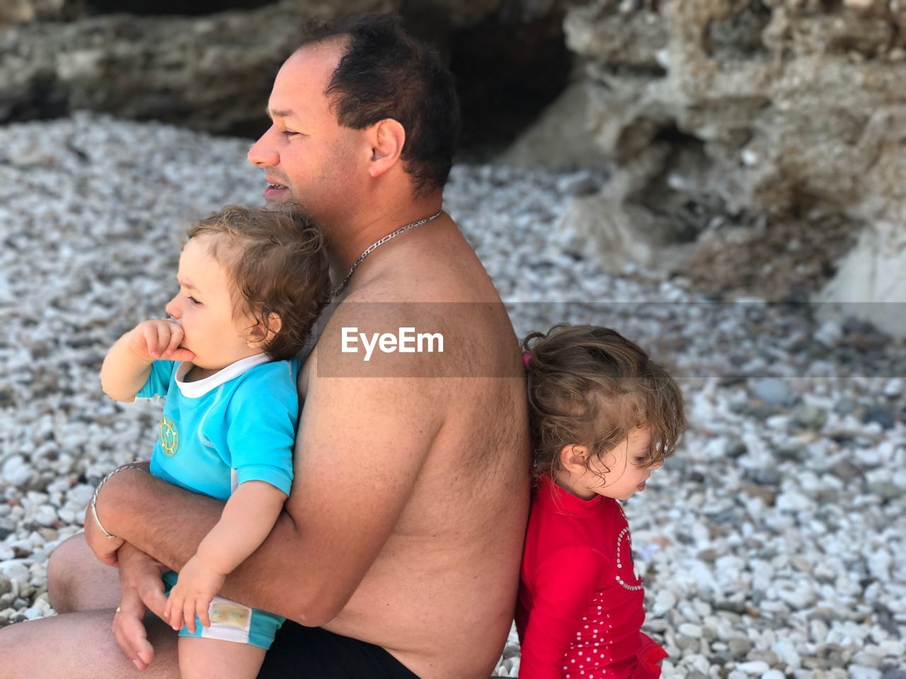 Shirtless man with children sitting at beach
