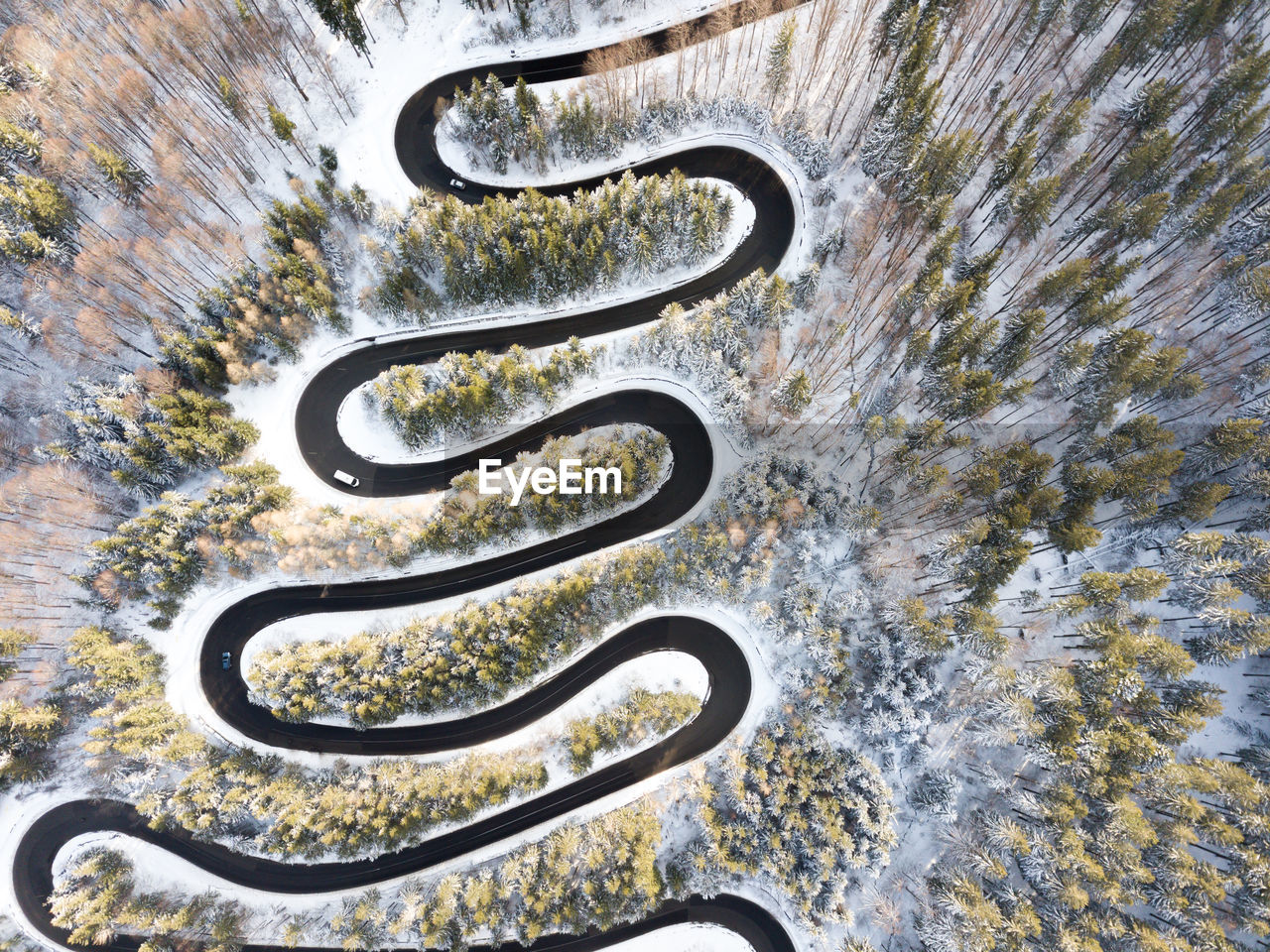 Curvy windy road in snow covered forest, top down aerial view