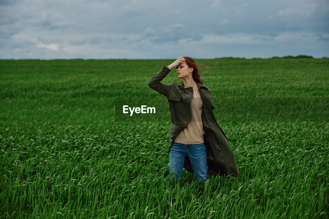 full length of young woman using phone while standing on field