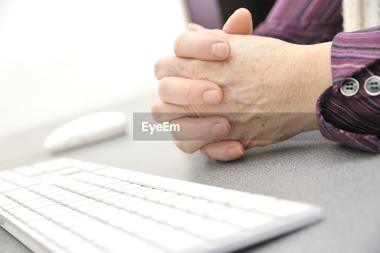 Cropped image of person with hands clasped by computer keyboard on table