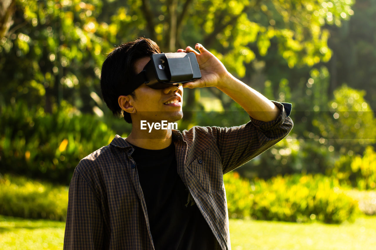 Young man looking through virtual reality while standing at park