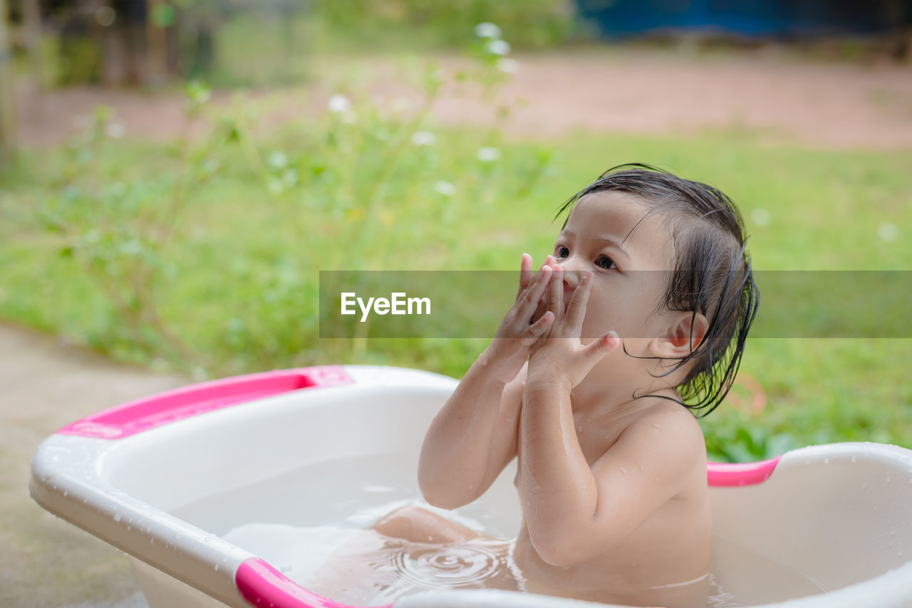 Cute baby girl looking away while sitting in bathtub at yard