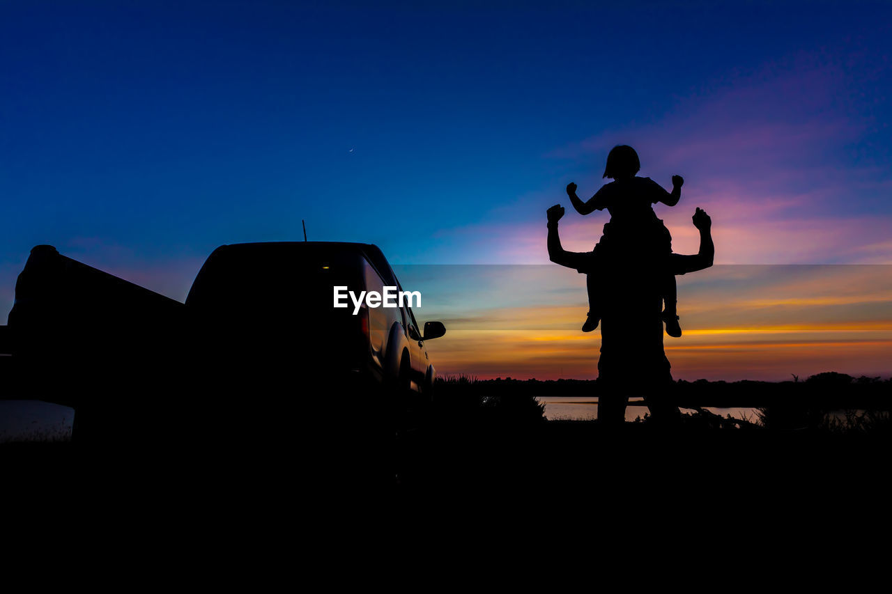 Silhouette father and son standing against orange sky during sunset