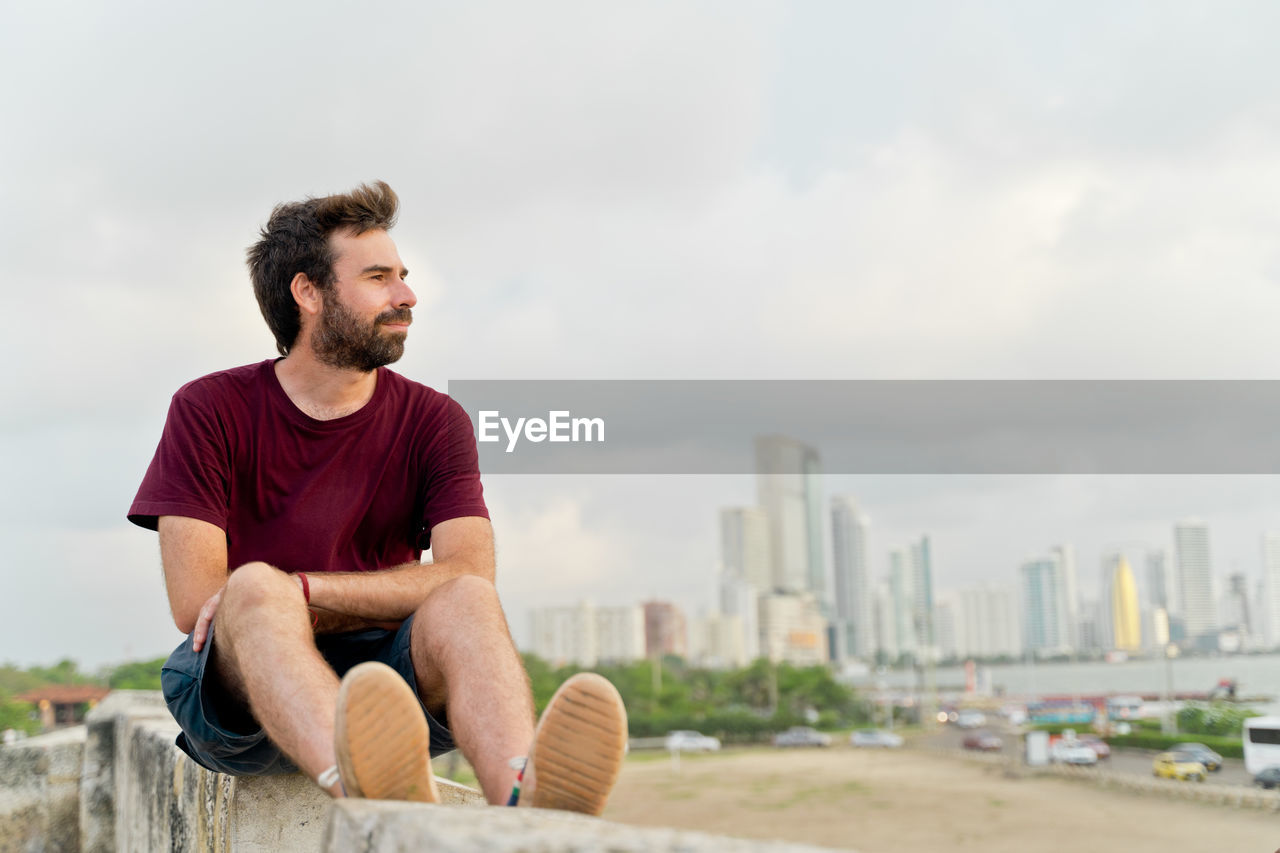 side view of young man sitting on street against sky