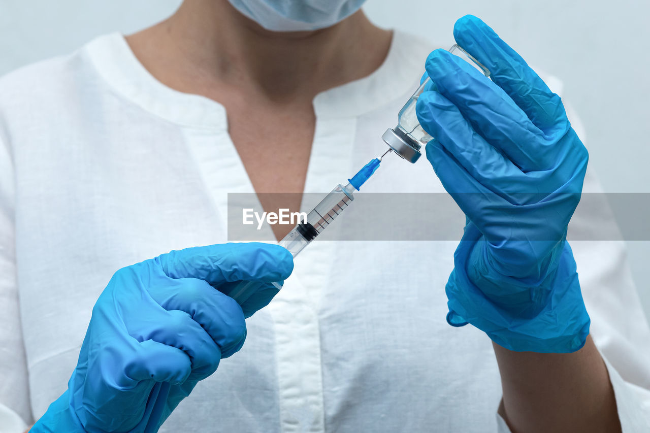 Midsection of doctor holding syringe with vial at hospital