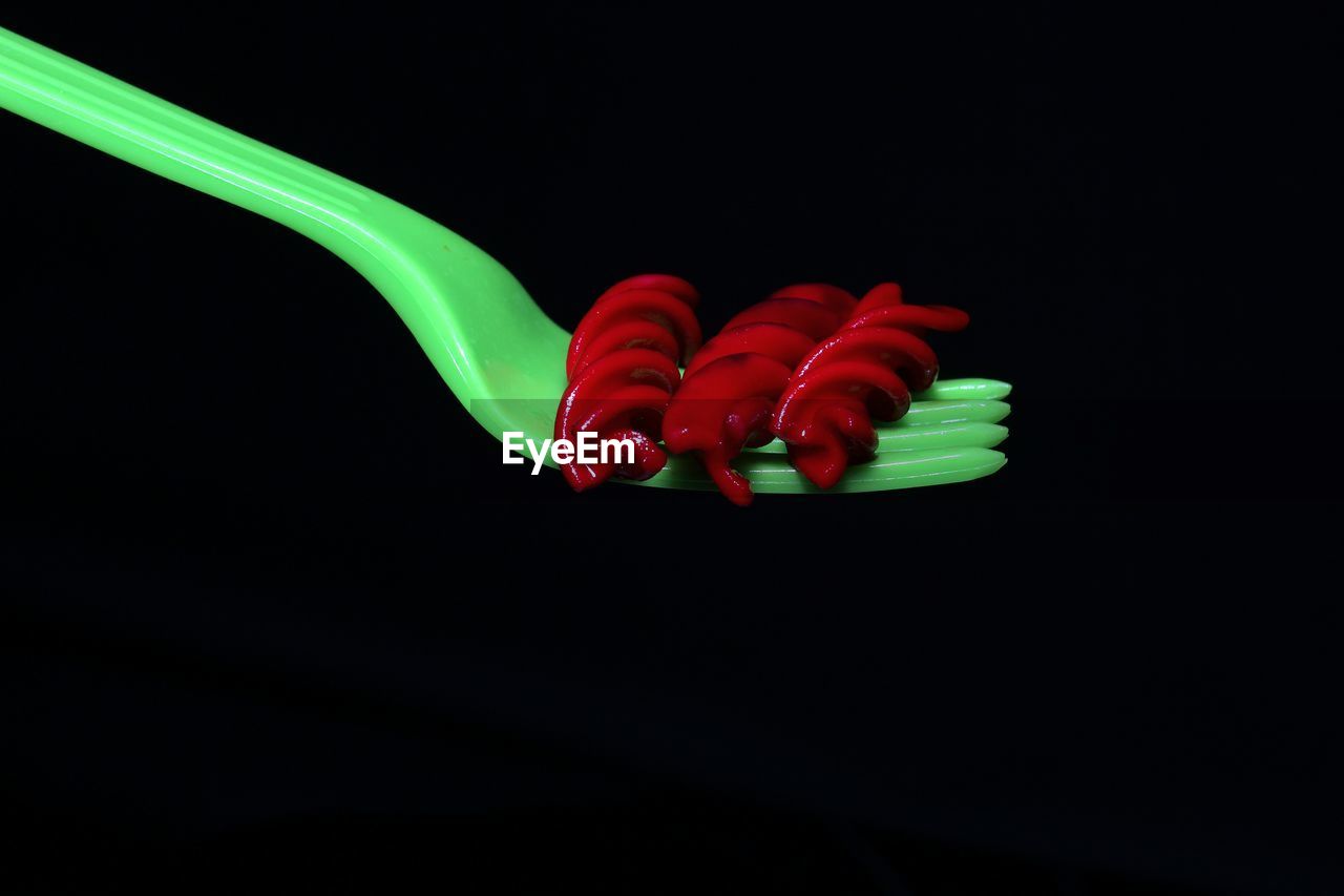 Close-up of red pasta on fork against black background