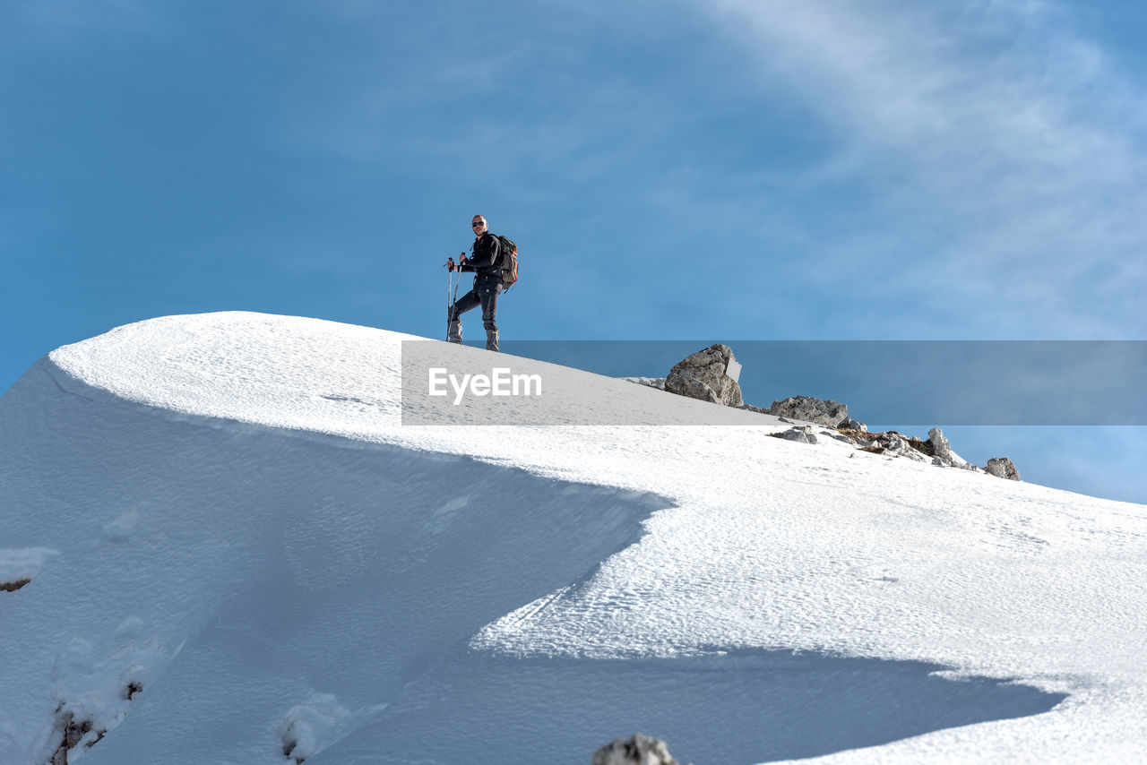 MAN CLIMBING ON SNOWCAPPED MOUNTAIN AGAINST SKY