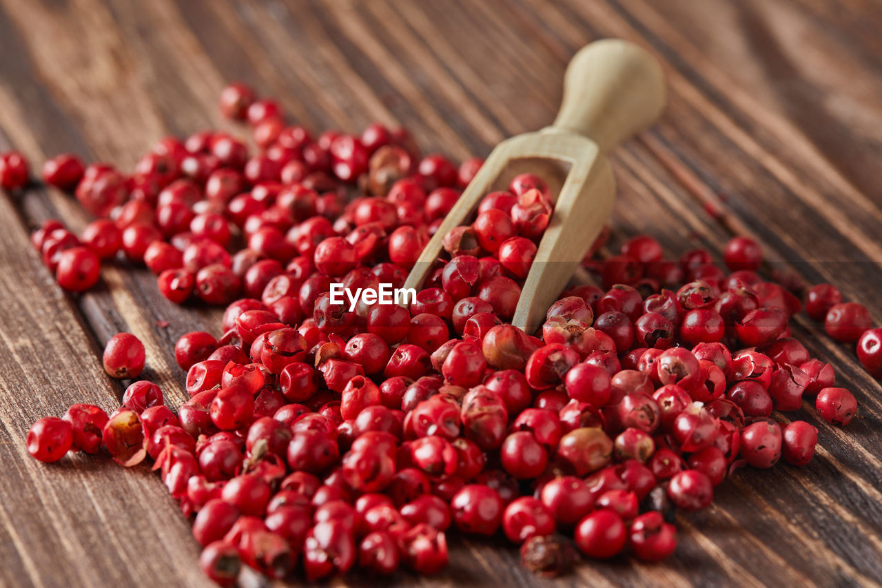 Red peppercorns with wooden spatula scattered on wooden vintage background