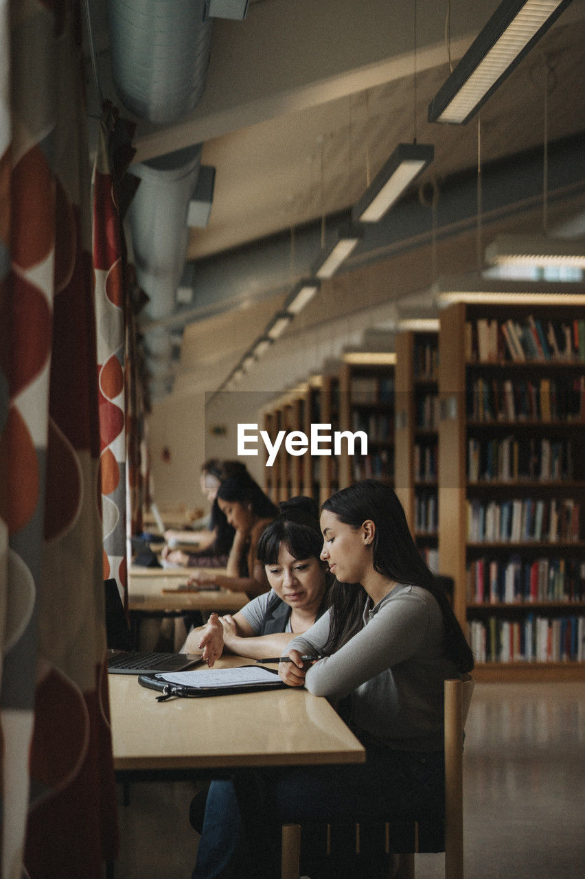 Professor and student discussing over book in library at university