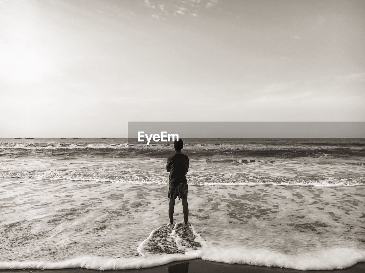 Rear view of man standing on shore against sky