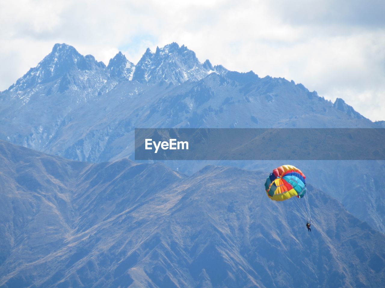 Person paragliding over mountain against sky