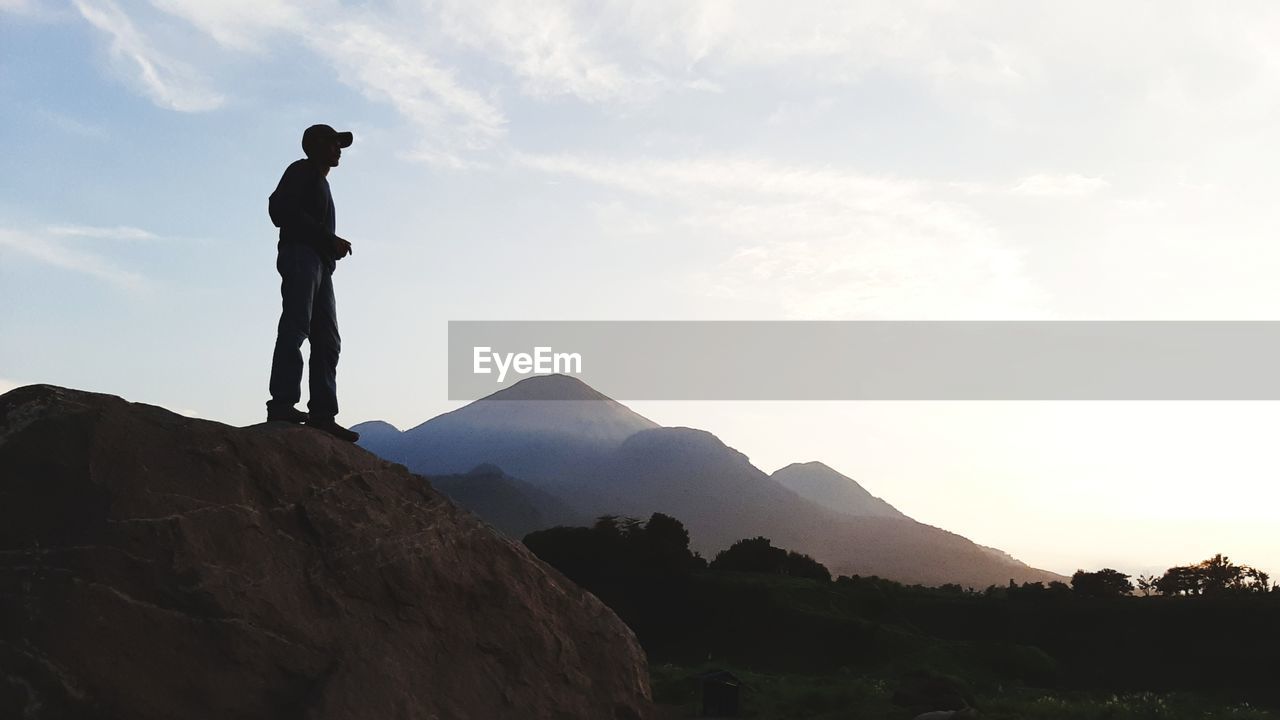 Silhouette man standing on rock against sky