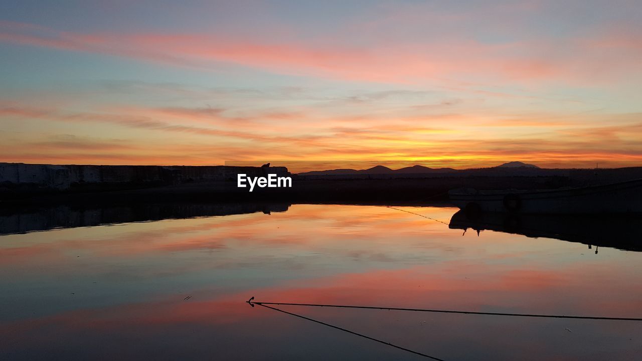 Scenic view of lake against dramatic sky during sunset