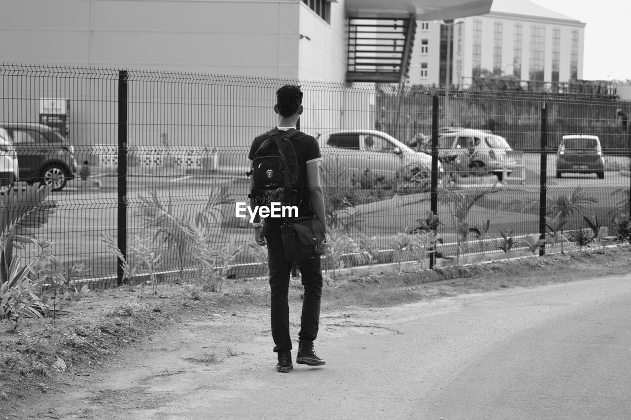 Rear view of man standing against buildings and cars