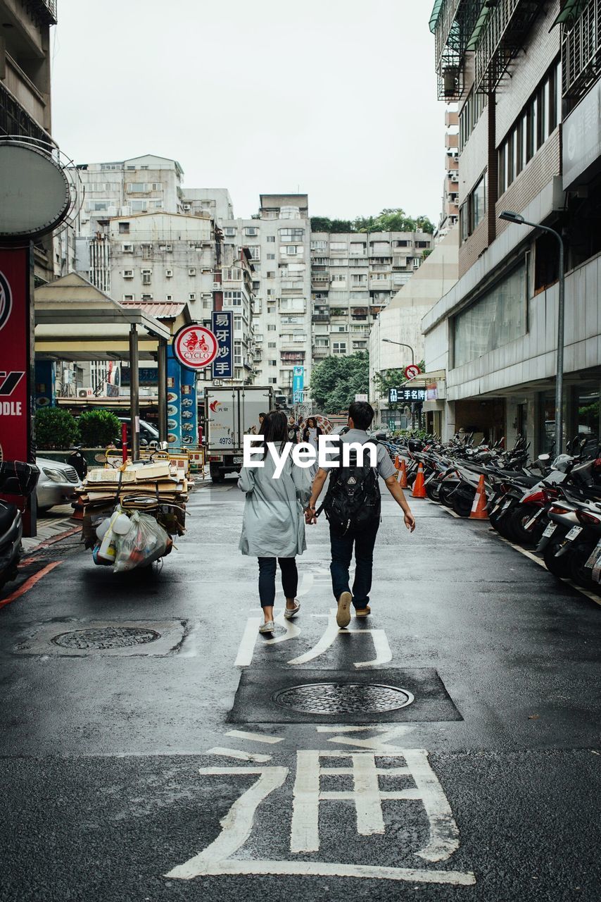 Rear view of couple walking on street in city