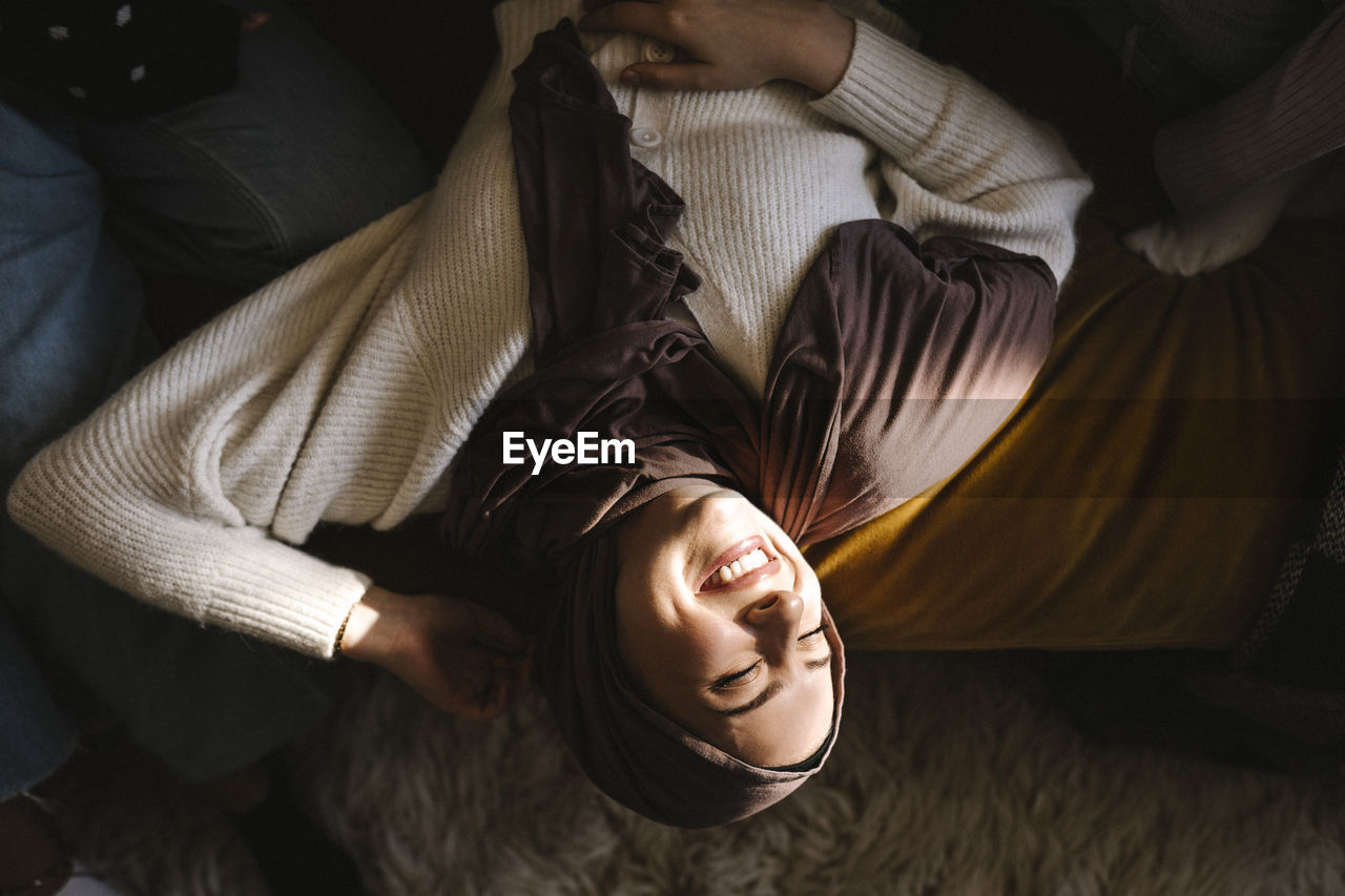 Smiling young woman with eyes closed lying by friends on sofa at home