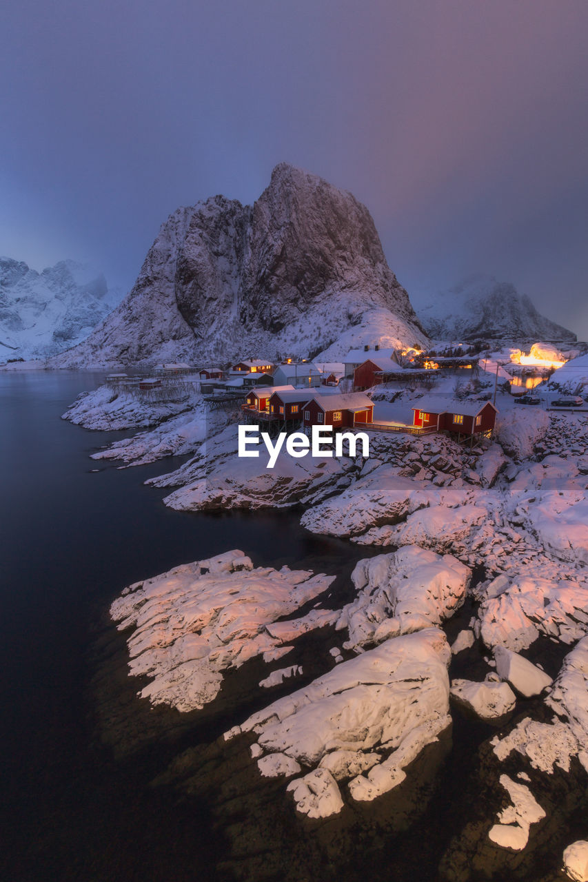 Houses and snowcapped mountains by lake at night