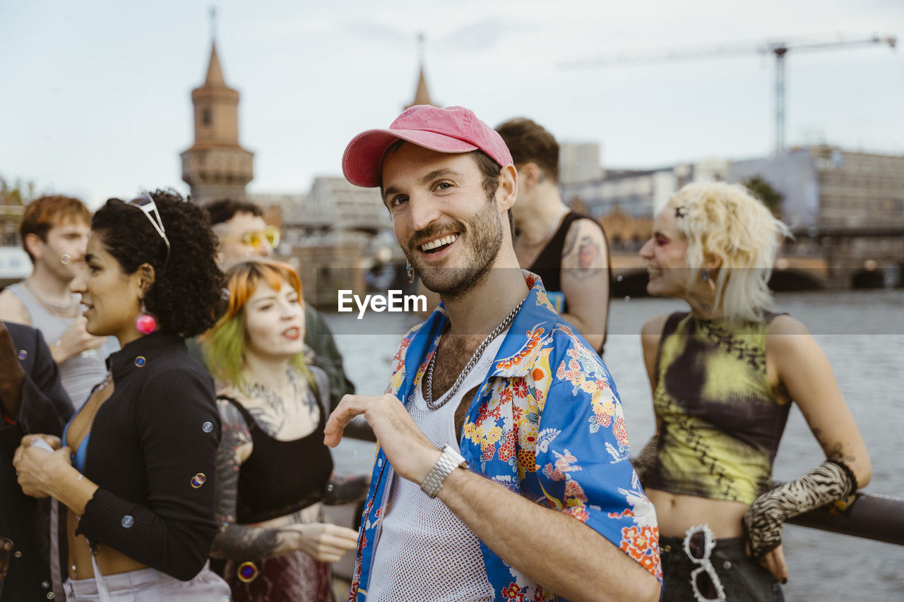 Portrait of smiling gay man wearing floral pattern and dancing with non-binary friends in city