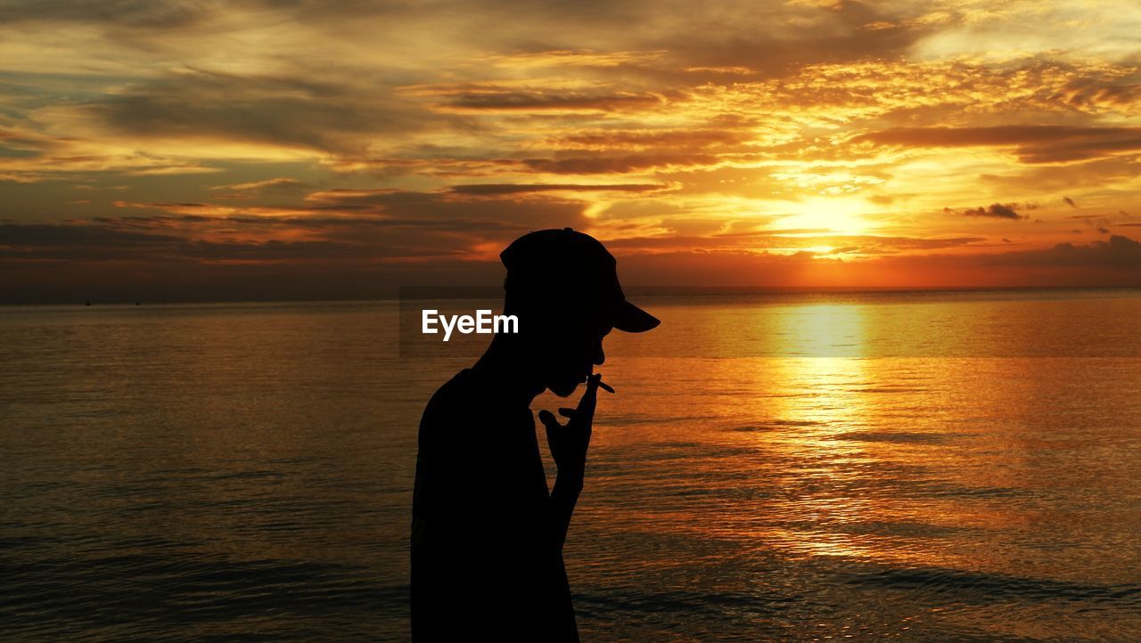 Silhouette man smoking against sea during sunset