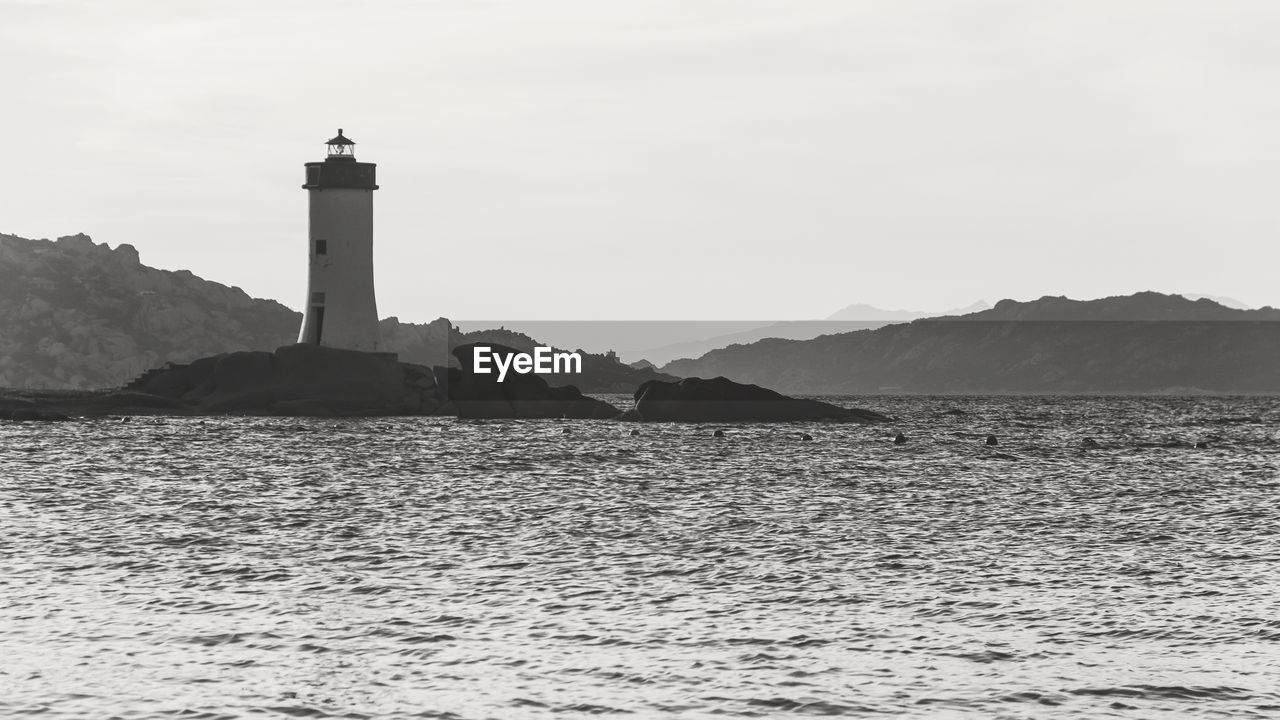 Monochrome landscape of lighthouse on the rocks and mountain on background during sunset