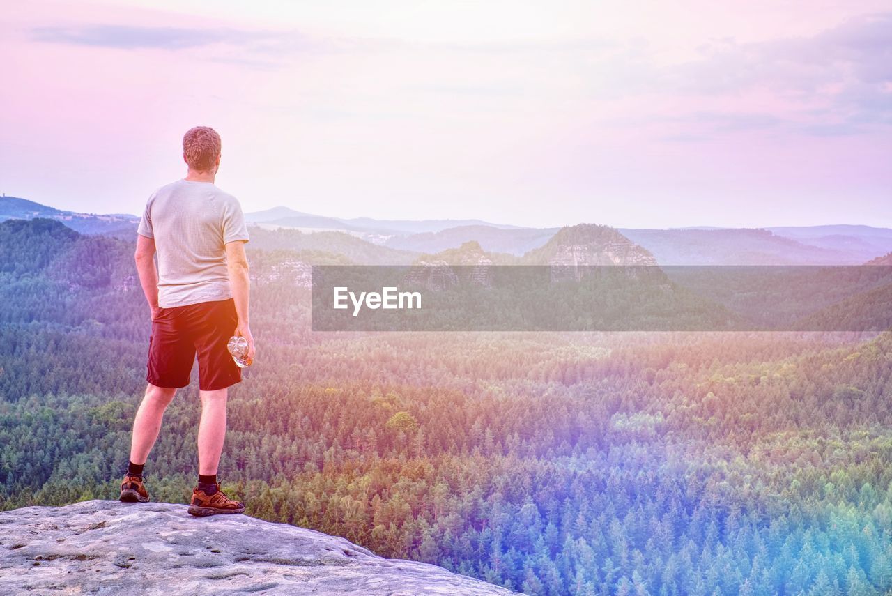 Hiker or running man hold plastic bottle with drink on rocky edge at misty mountains background