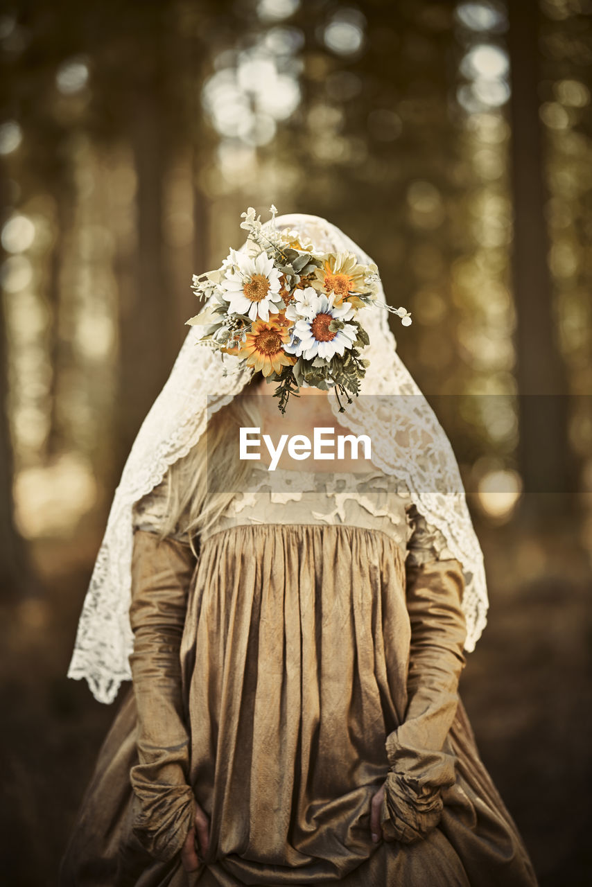 Bide with flower covering face standing in forest