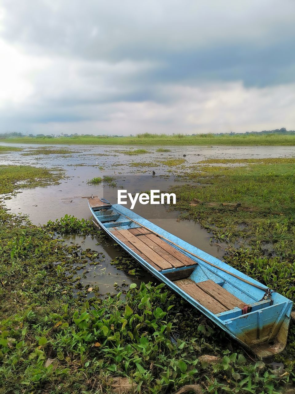 BOAT MOORED ON GRASS BY LAKE AGAINST SKY