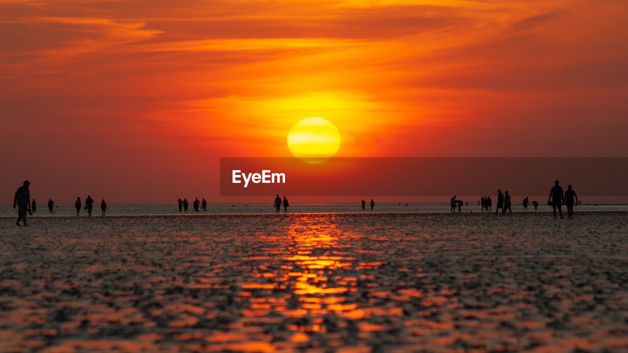 Silhouette people on beach against orange sky