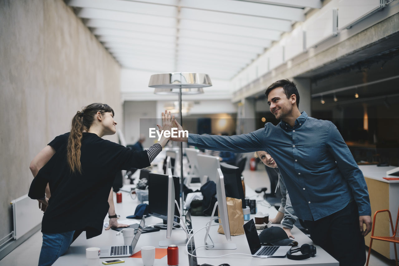 Male and female computer programmers giving high-five over desk in office