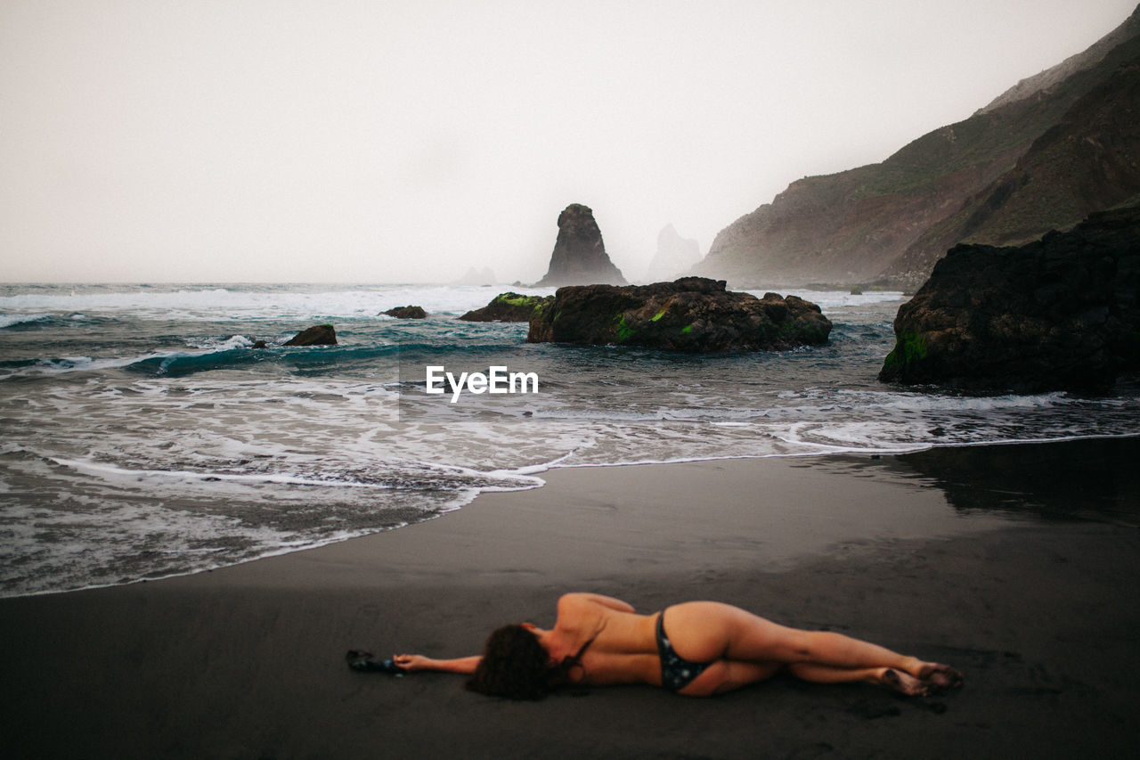 Rear view of woman lying on shore at beach against sky