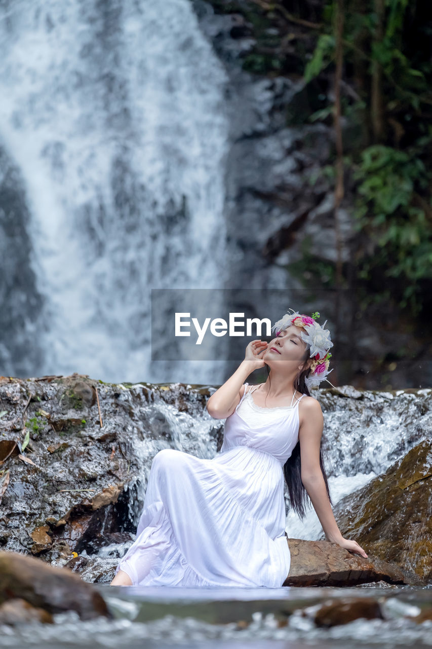 A beautiful young lady relaxes in nature near a waterfall.