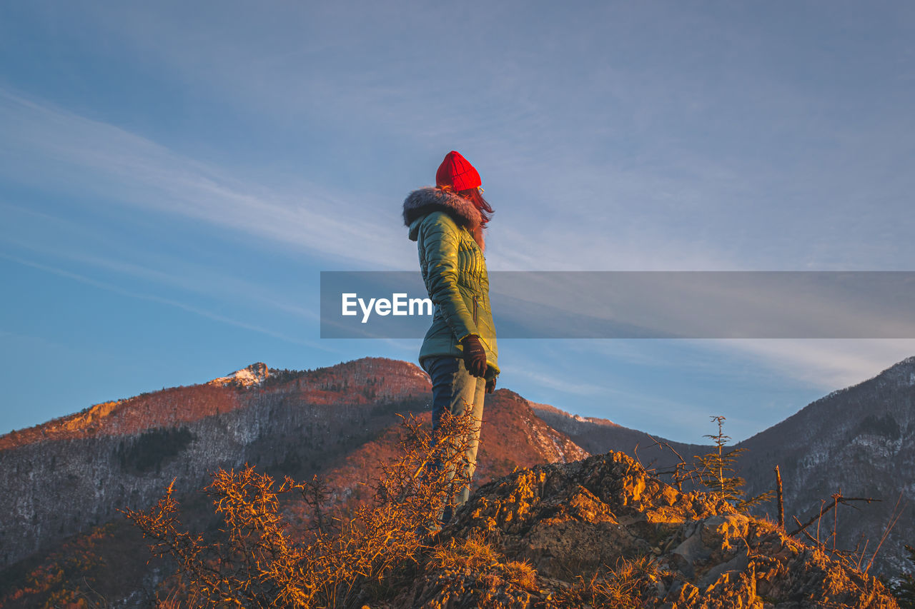 A young caucasian redhead woman standing in the french alps mountains in winter at sunset