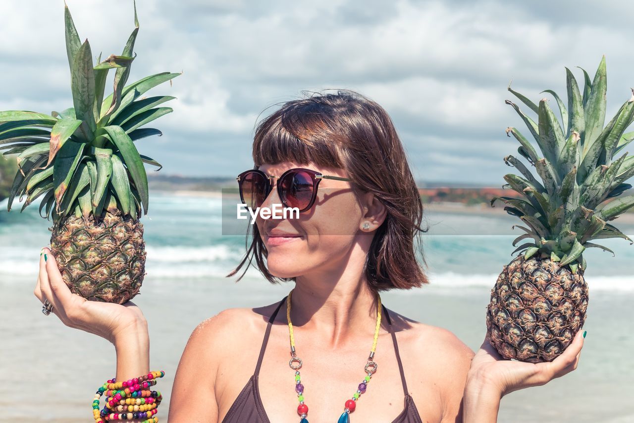 Smiling young woman holding pineapples at beach