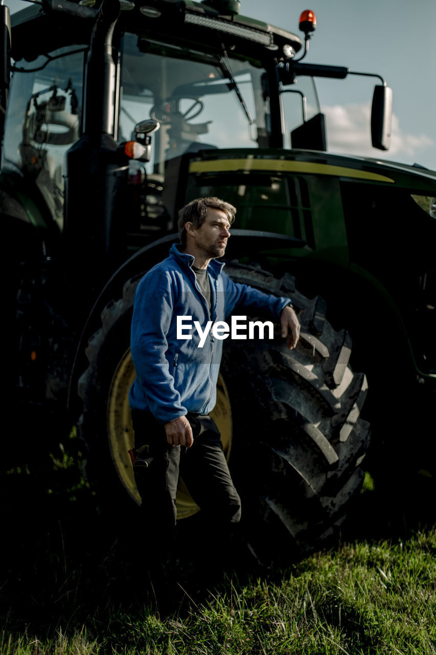 Contemplative farmer standing by tractor at farm