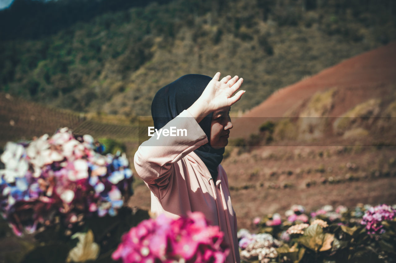 Woman gesturing while standing amidst flowers against mountains