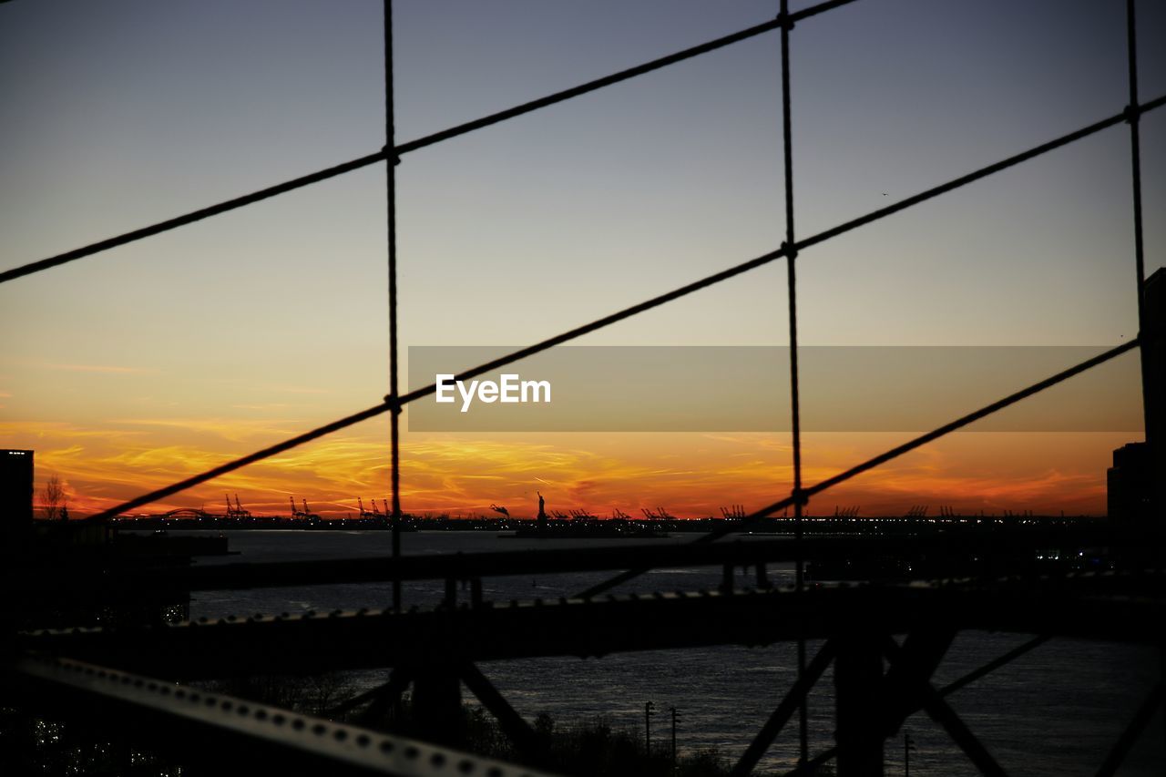 Silhouette bridge over river against sky during sunset