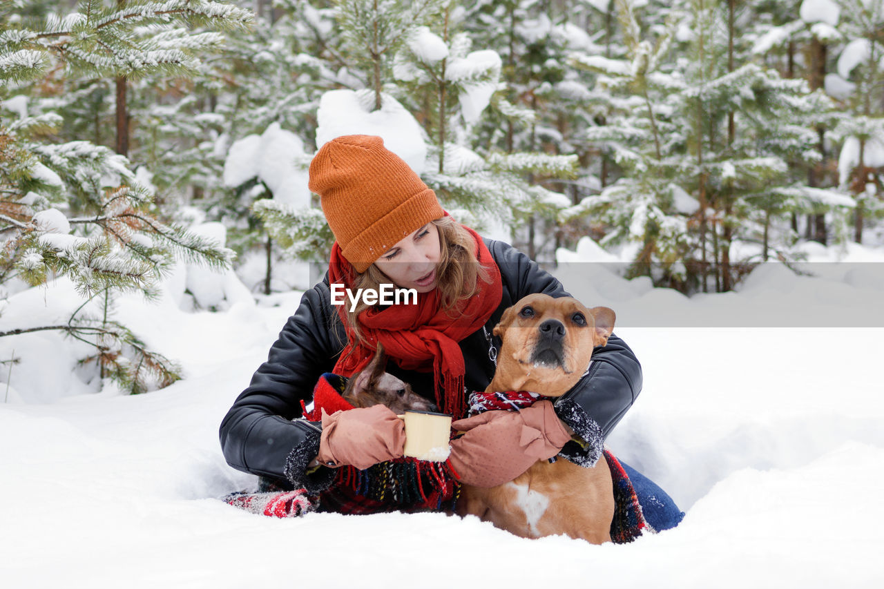 Woman with dogs on snow field against trees during winter