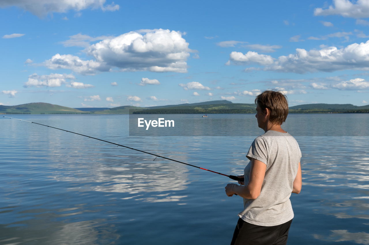 A woman fisherman catches fish for a bait from a blue lake on the background of a mountainous coast.