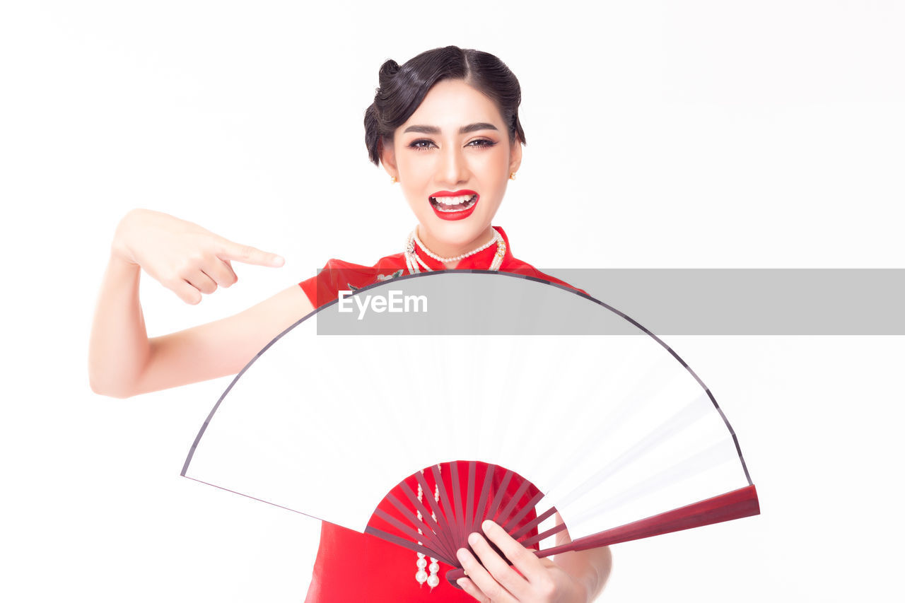 Portrait of smiling woman pointing at hand fan against white background