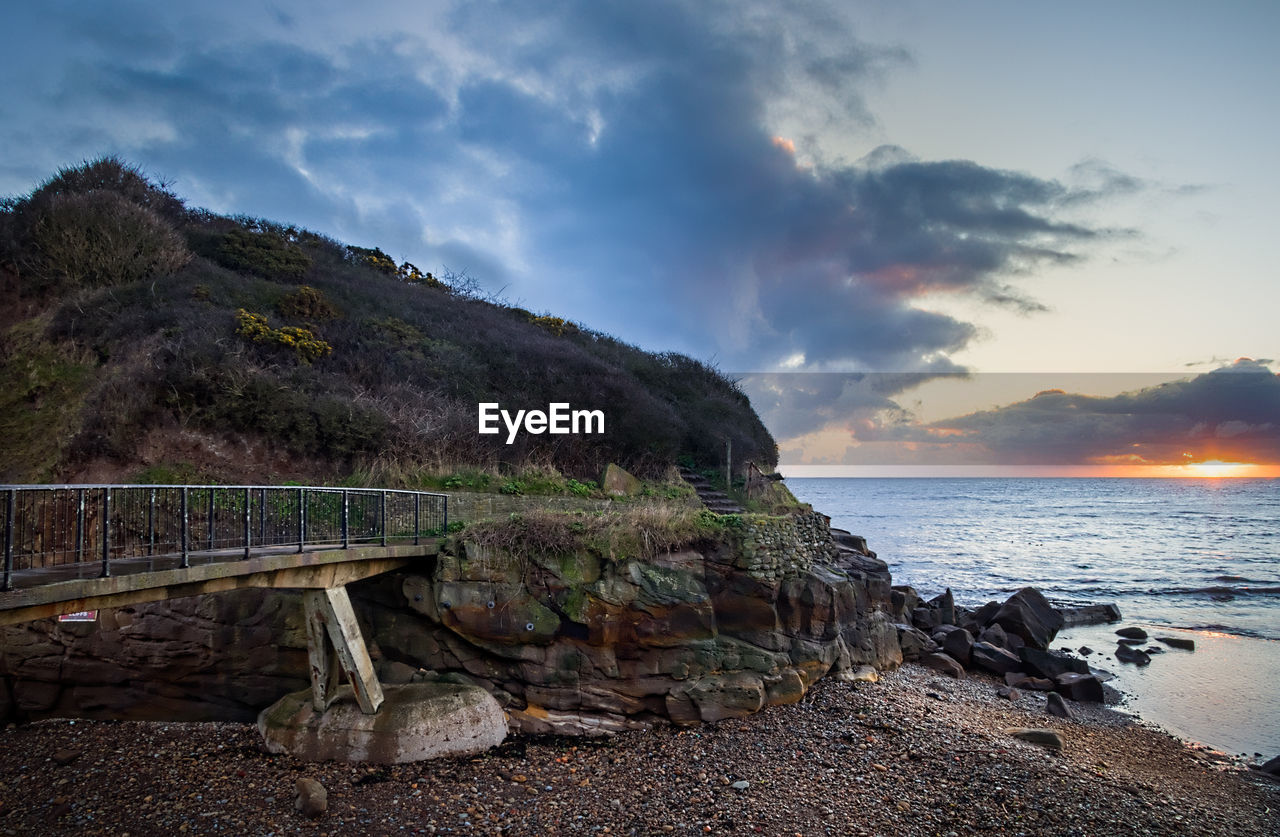 Bridge at beach by sea against sky during sunset